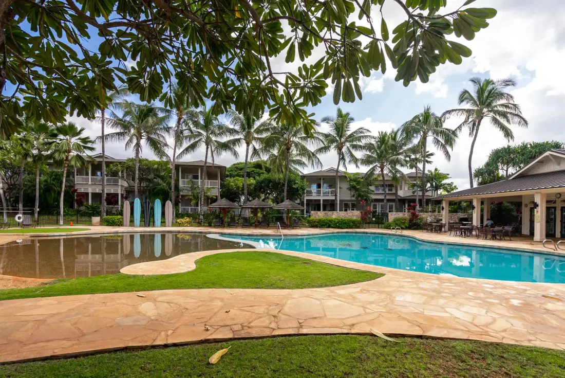 An outdoor swimming pool sits beside palm trees and a paved deck.