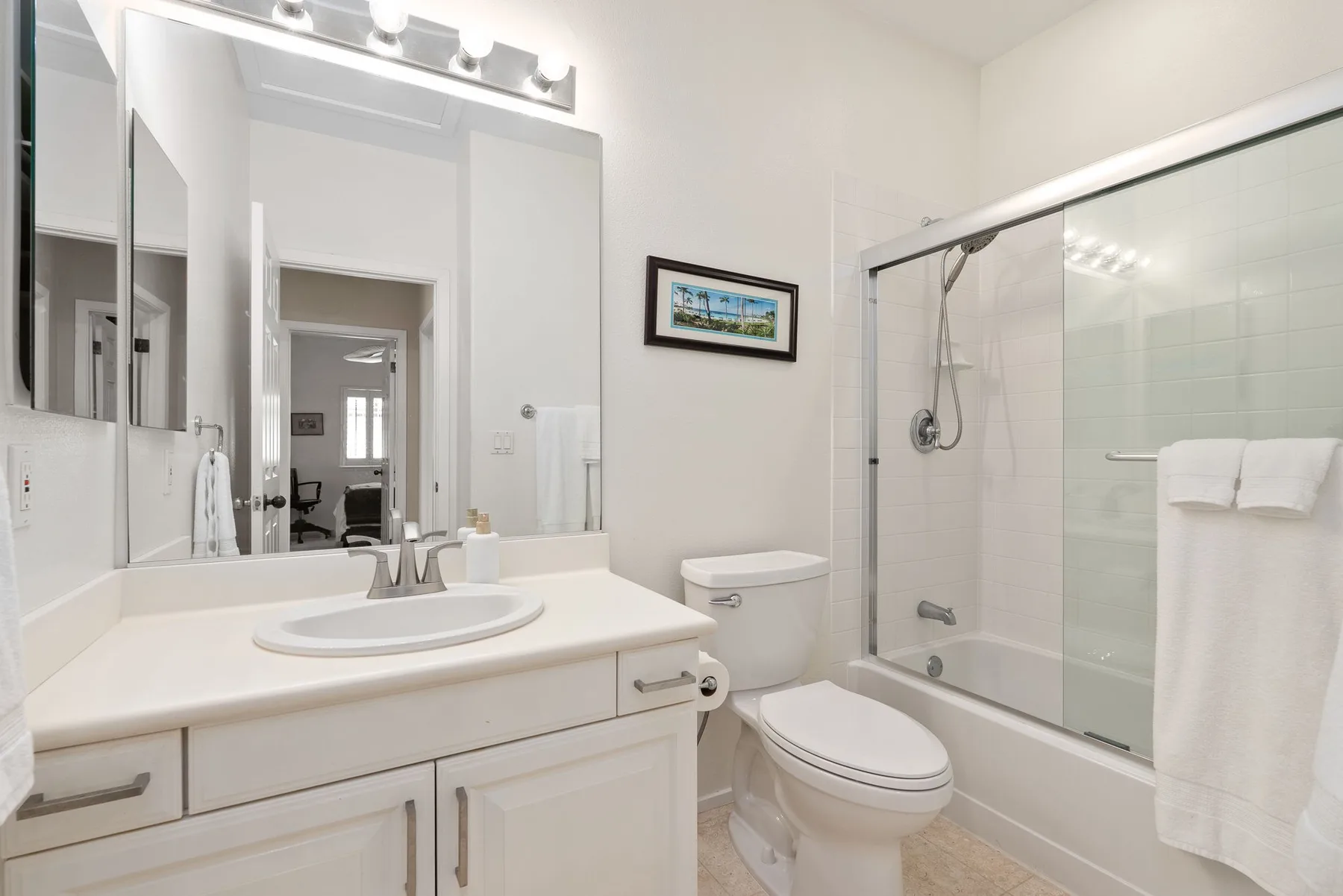 A bright bathroom with a sink, vanity, toilet, and bathtub with a glass shower screen.