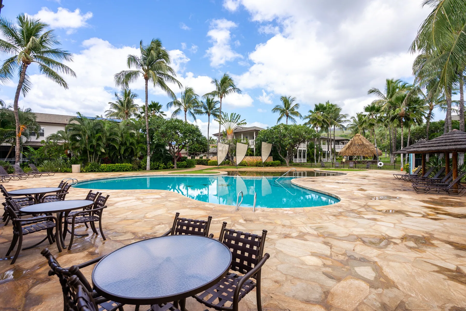 An outdoor swimming pool is surrounded by palm trees and patio seating.