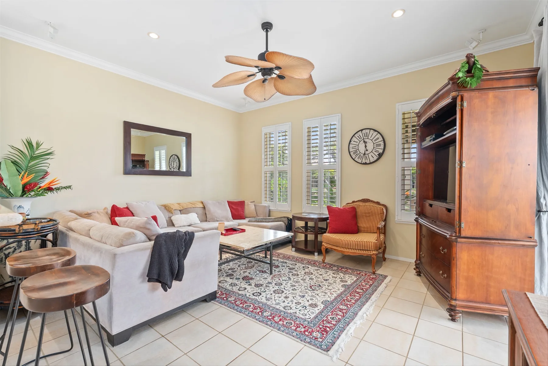 A living room with light seating, a patterned rug, and a wooden entertainment cabinet.