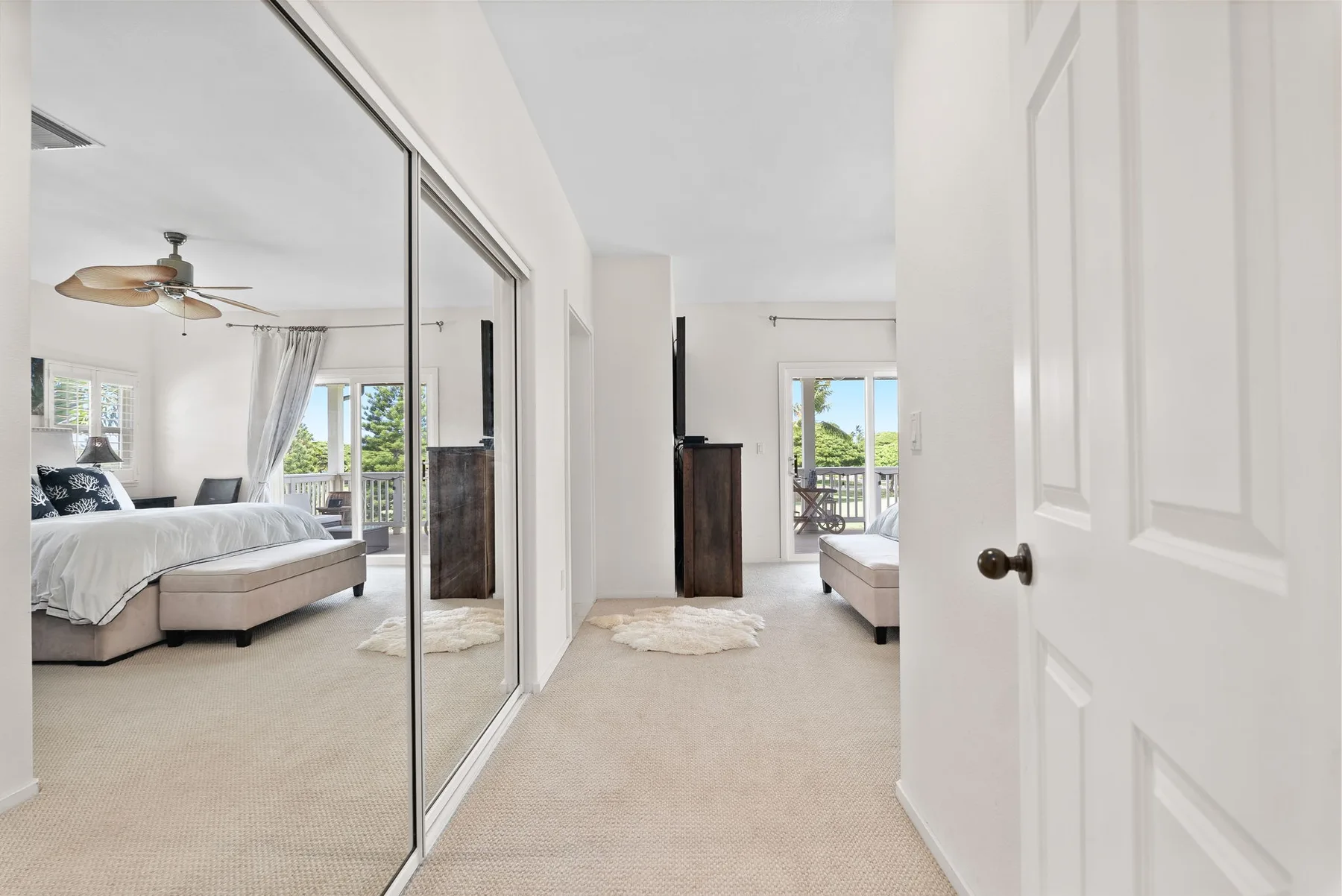 A bright bedroom with mirrored closet doors and a view of the bed.