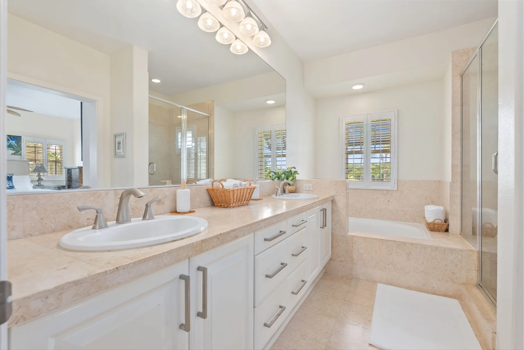 A bright bathroom with a long vanity, large mirror, and bathtub.