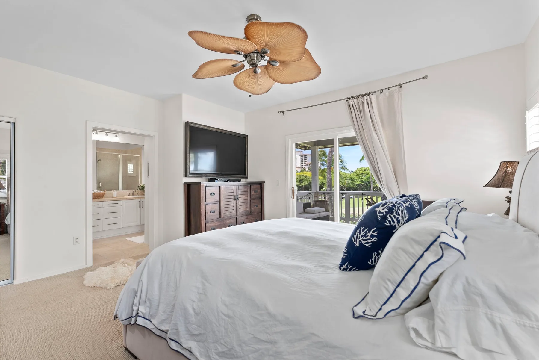 A bright bedroom with a bed, television, and sliding glass doors opening onto a balcony.