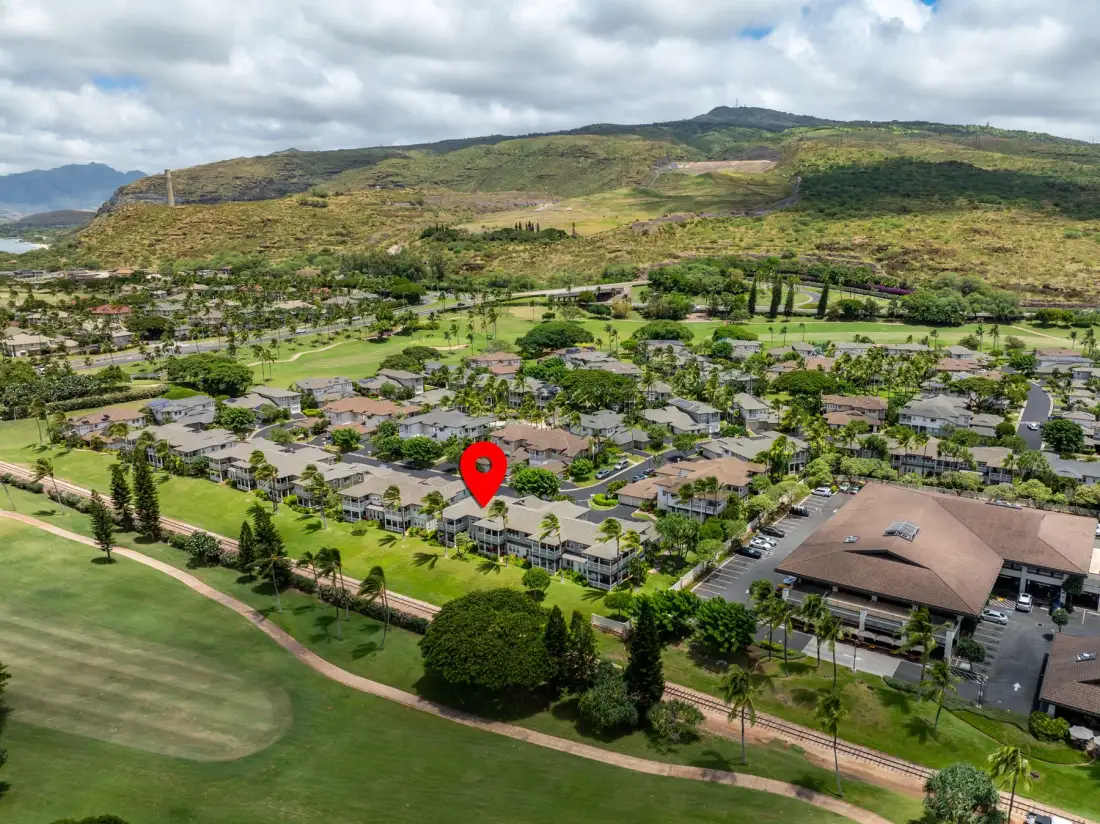 Aerial view of a residential neighborhood beside green hills and open lawns.