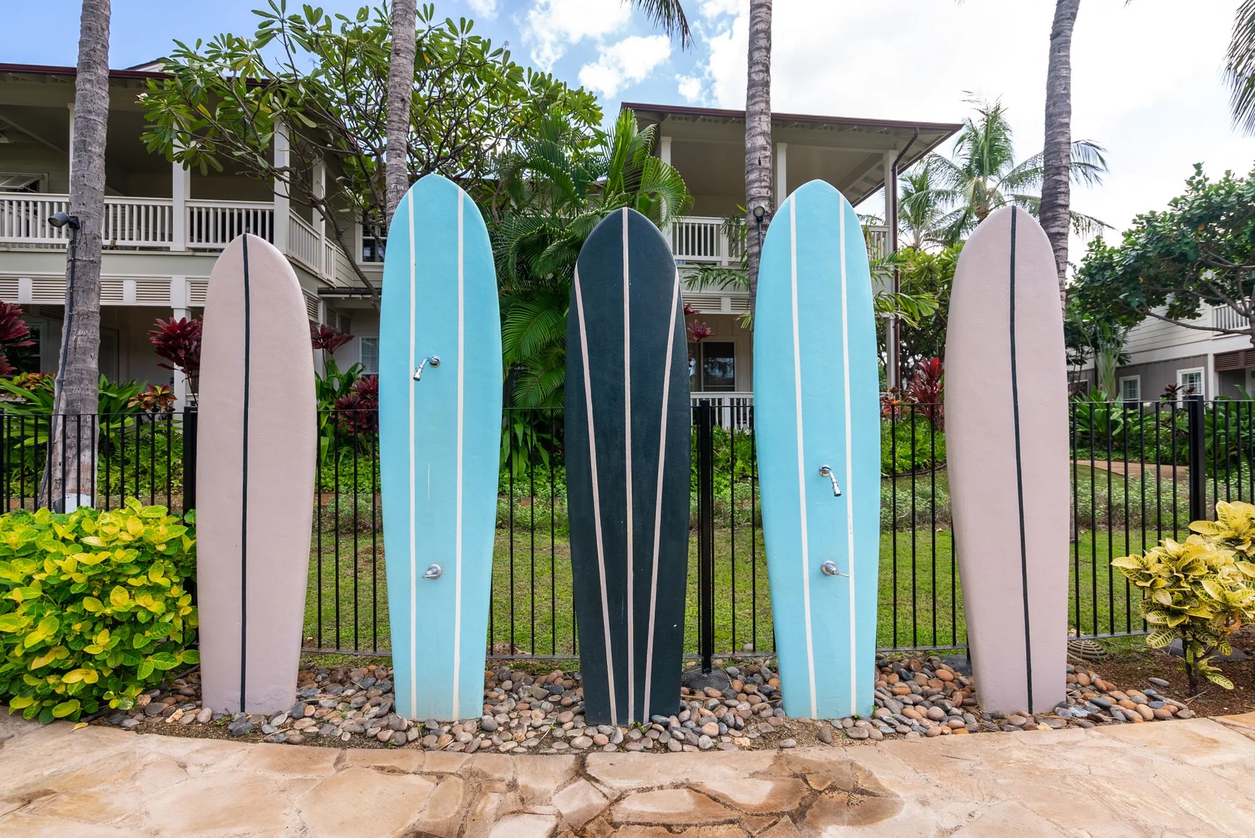 Surfboards line a black fence in front of a tropical-style building.