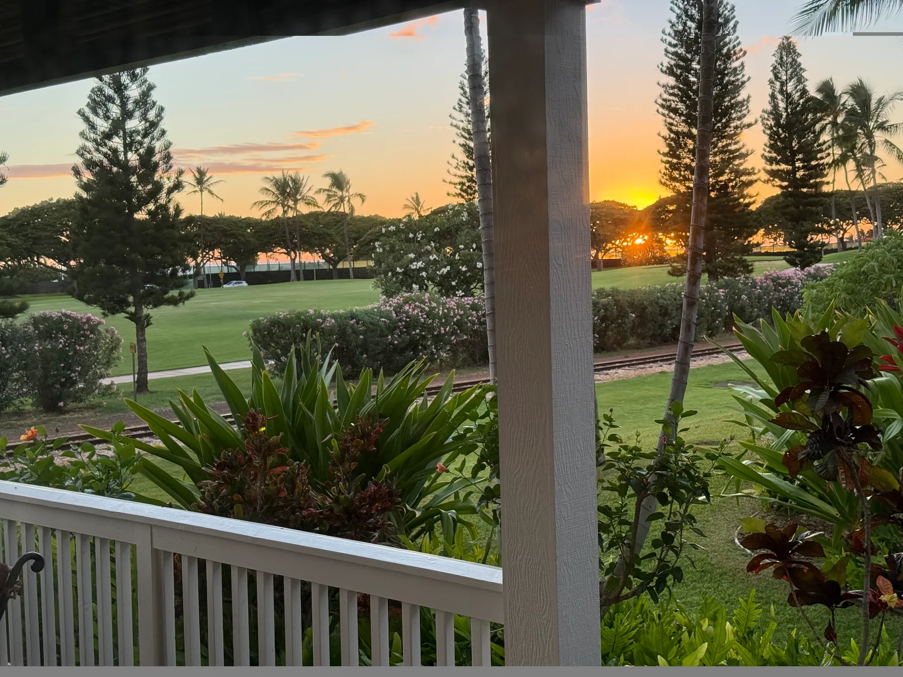 A sunset over a landscaped lawn and garden, viewed from a covered porch.