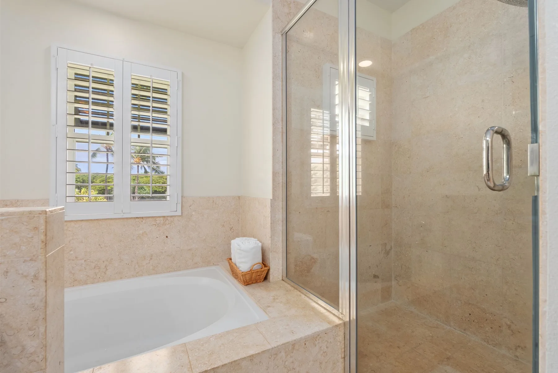 A bathroom with a bathtub beneath a shuttered window and a glass shower.