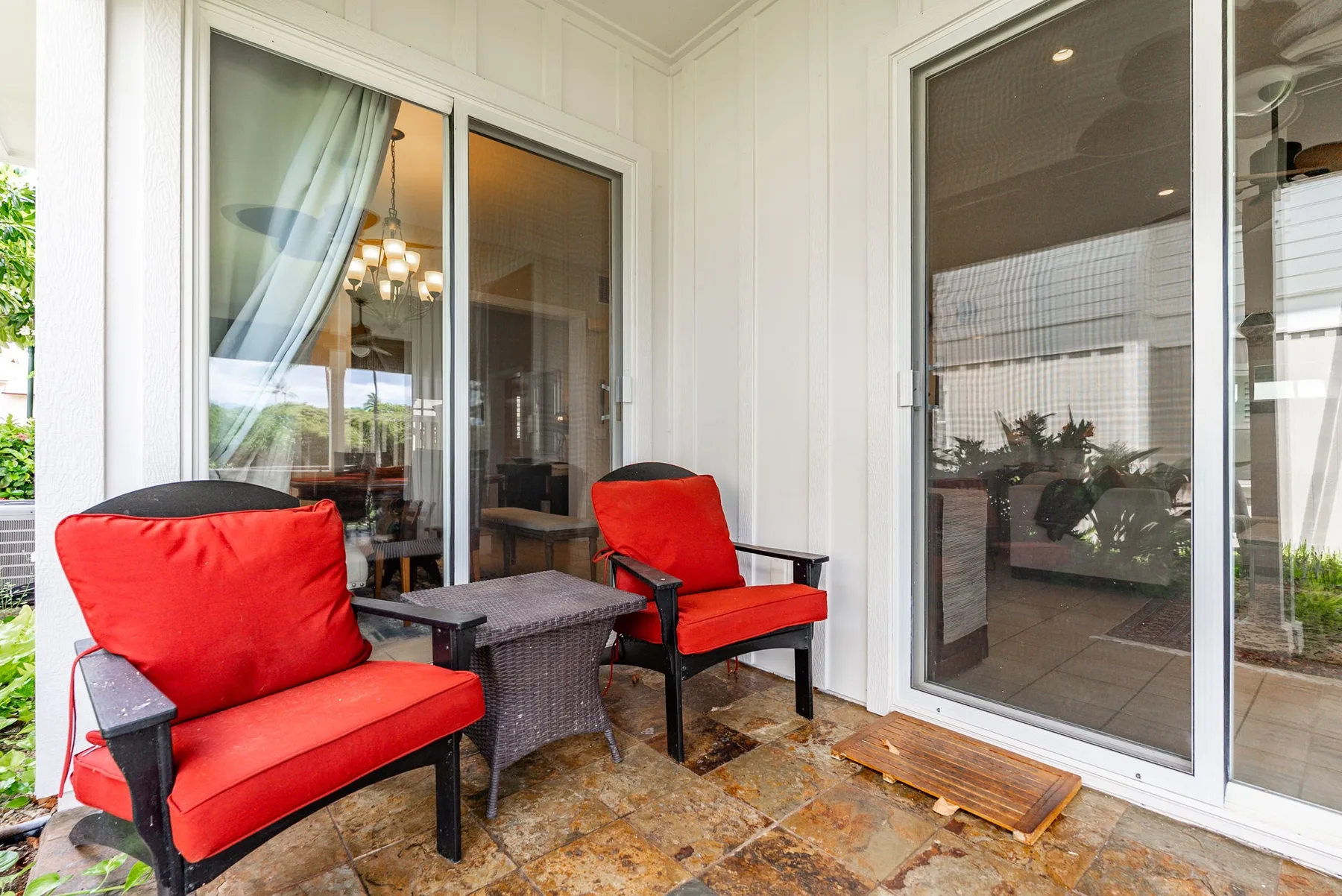 A covered patio with red seating and a small table beside glass doors.