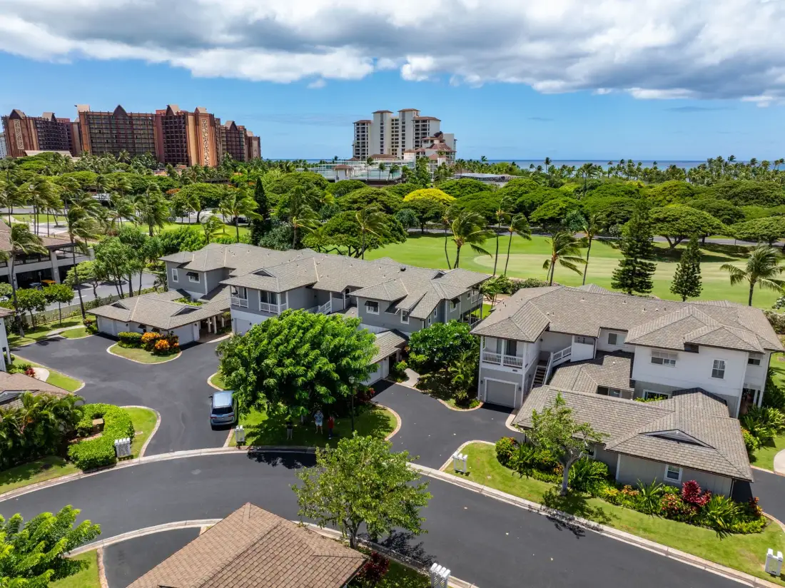 Aerial view of residential buildings amid green landscaping, with the ocean in the distance.