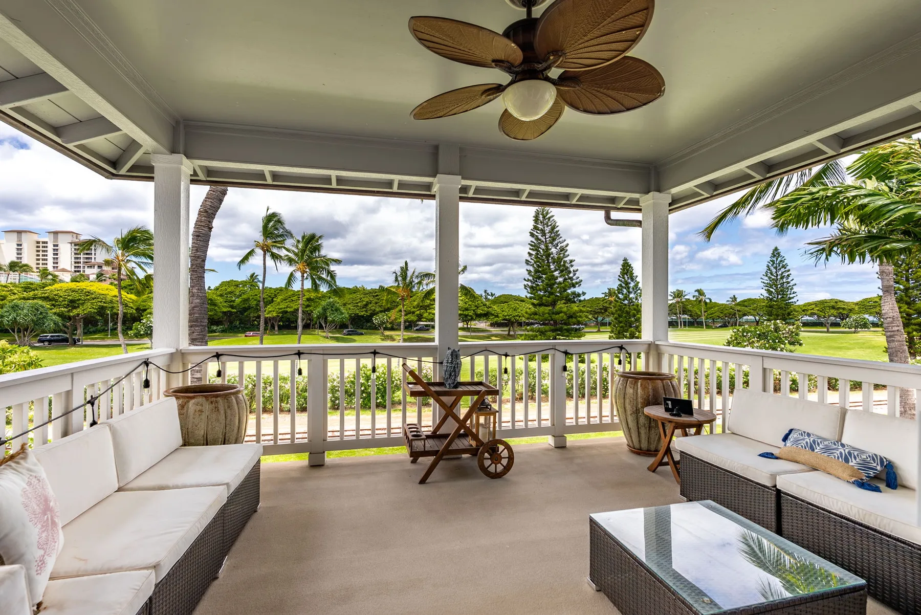 A covered outdoor seating area overlooks a green lawn and palm trees.