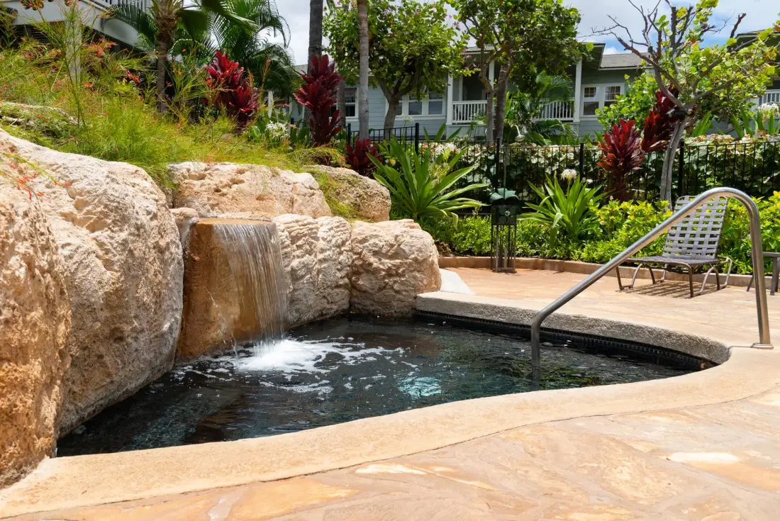 A small outdoor pool with a rock waterfall, surrounded by tropical plants.