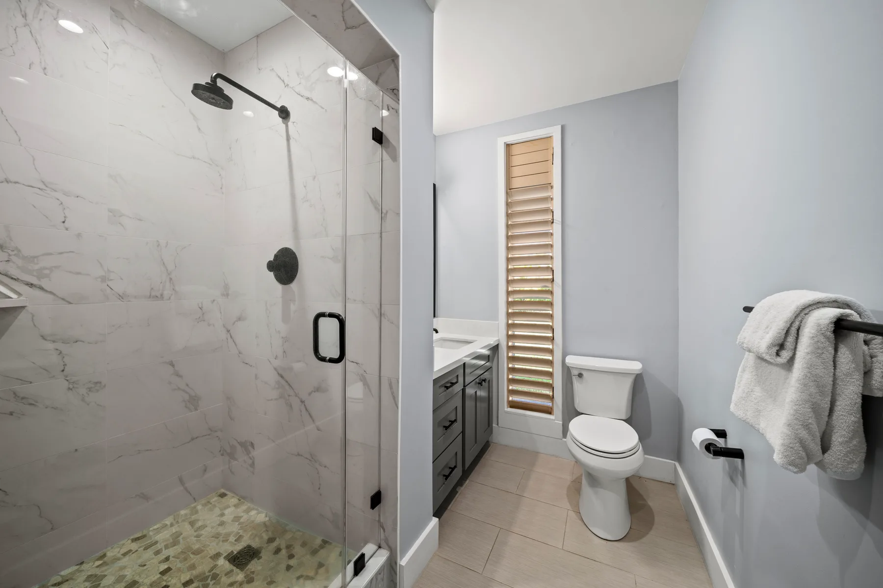 Un baño con ducha de vidrio, tocador, inodoro y una ventana estrecha.