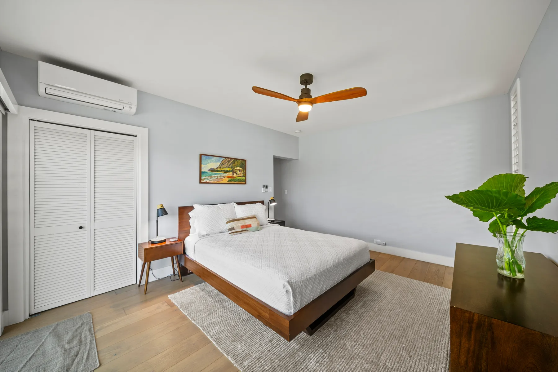 Un dormitorio luminoso con una cama, un ventilador de techo y una planta en maceta.