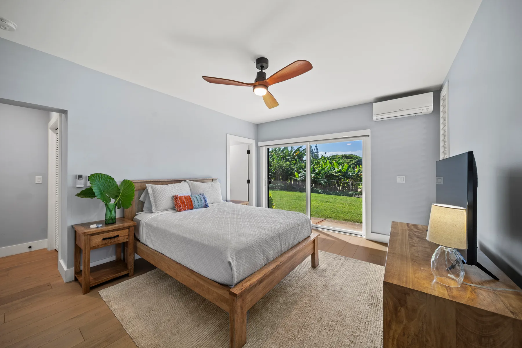 Un dormitorio luminoso con una cama de madera y puertas corredizas de vidrio hacia un jardín verde.