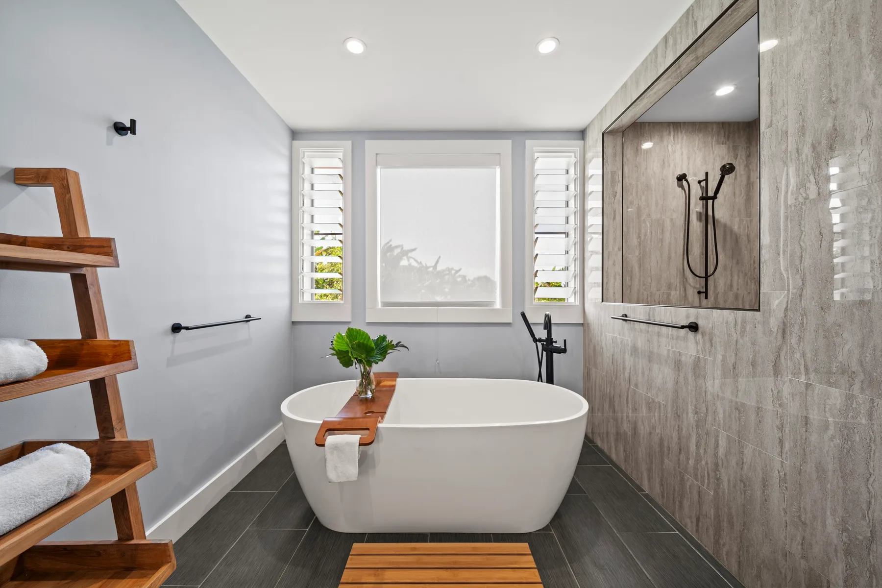 Un baño moderno tiene una bañera independiente bajo una ventana grande.