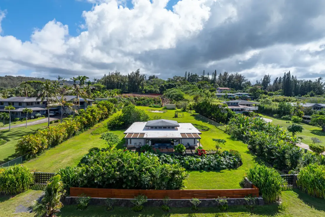 Vista aérea de una casa rodeada de césped verde y vegetación tropical.