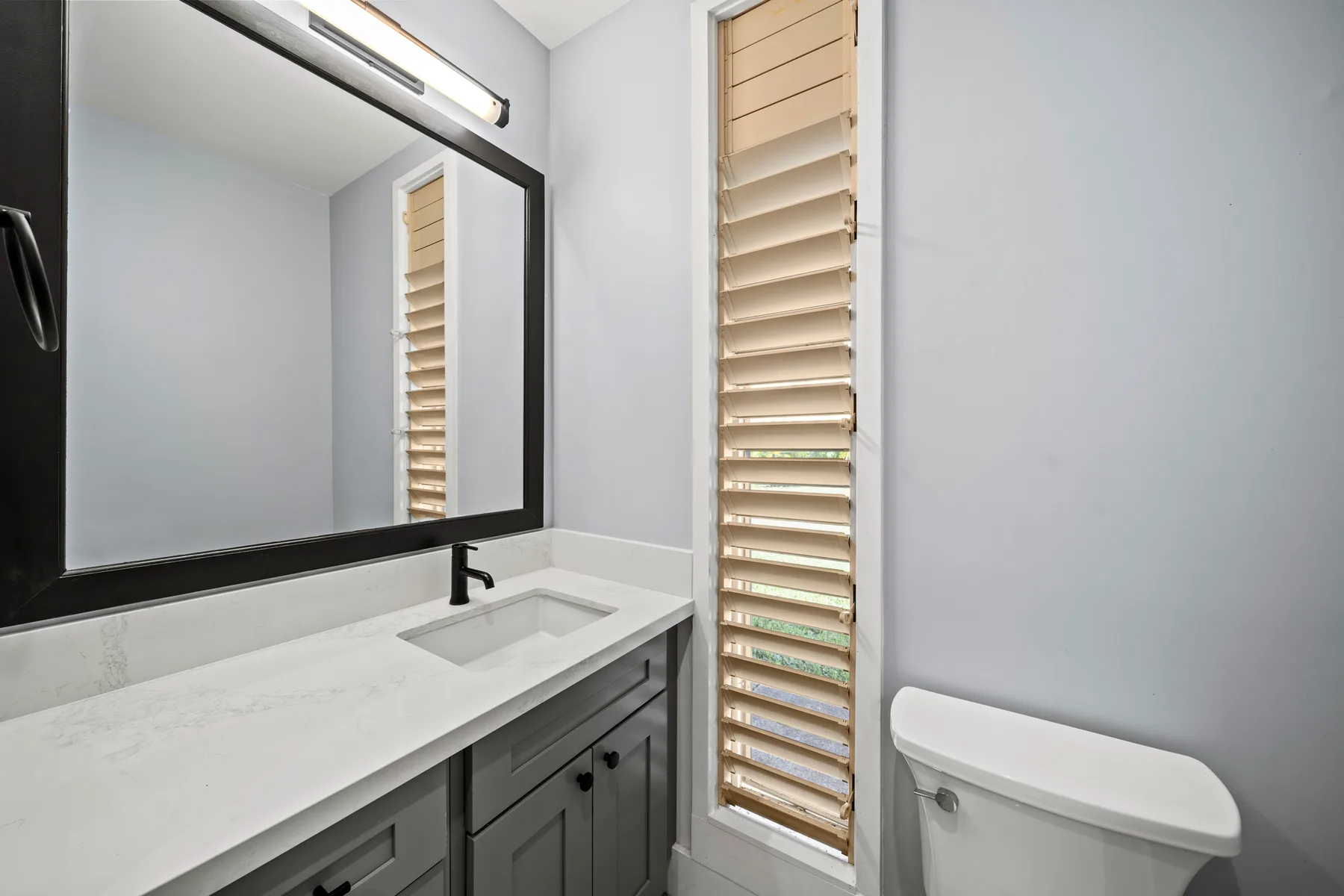 Un lavabo de baño con espejo y una ventana con persianas.