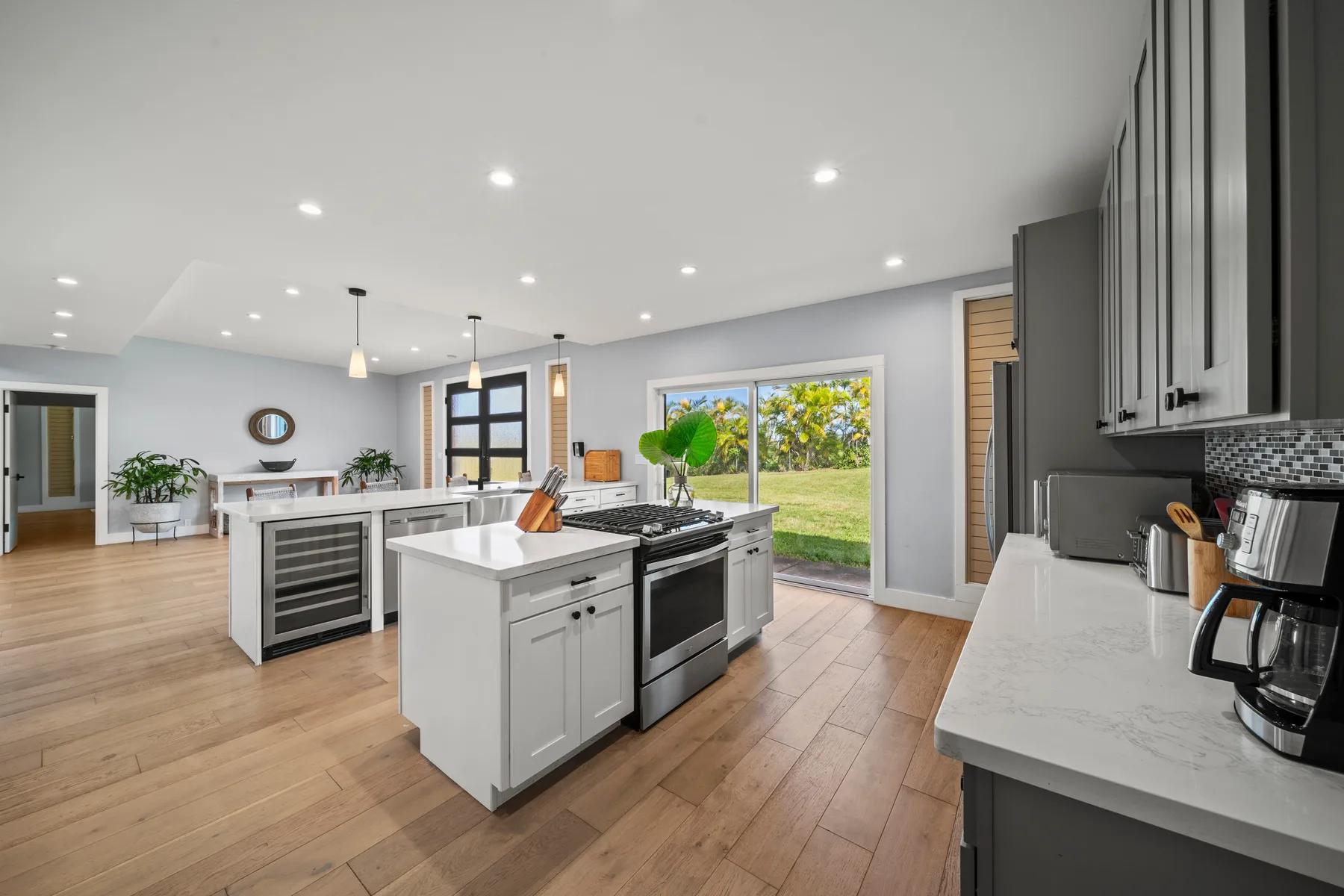 Una cocina luminosa con islas centrales, gabinetes oscuros y ventanas grandes.