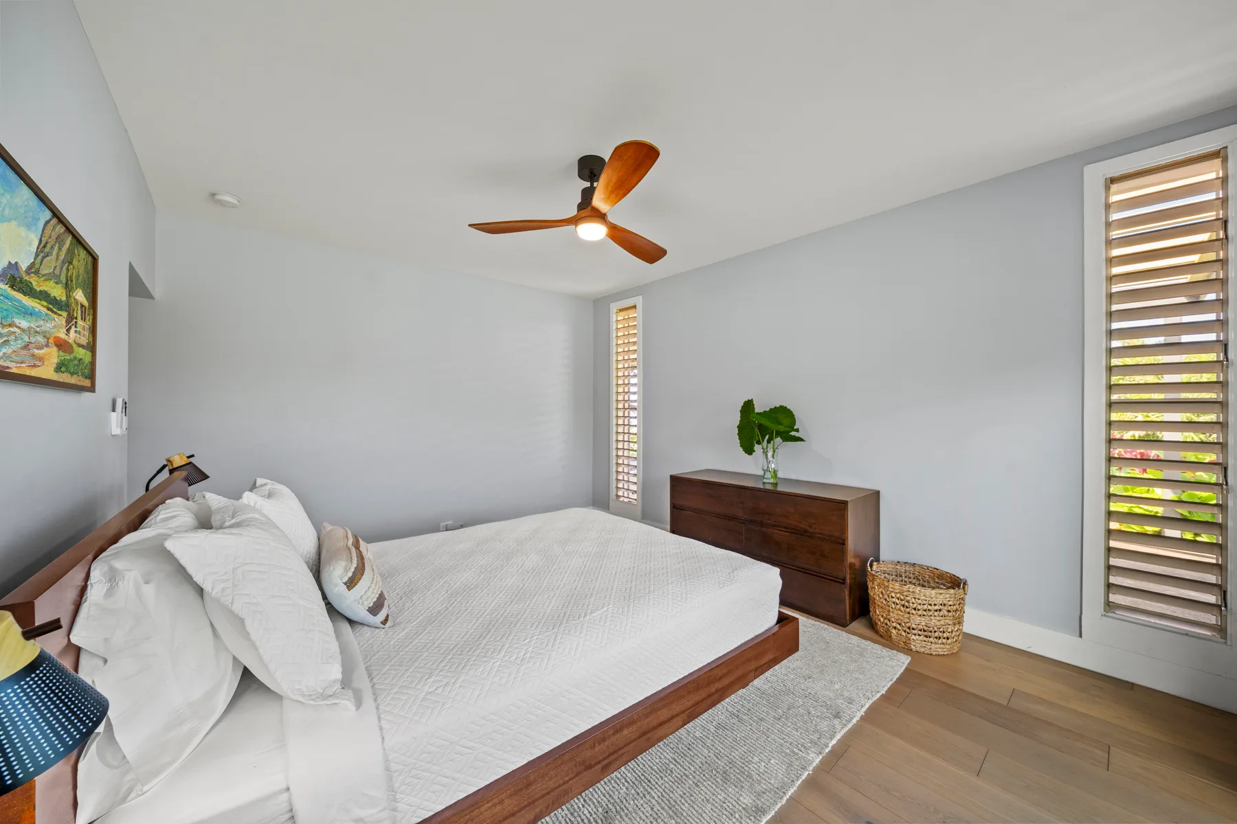 Un dormitorio luminoso con una cama, una cómoda de madera y ventanas con persianas.