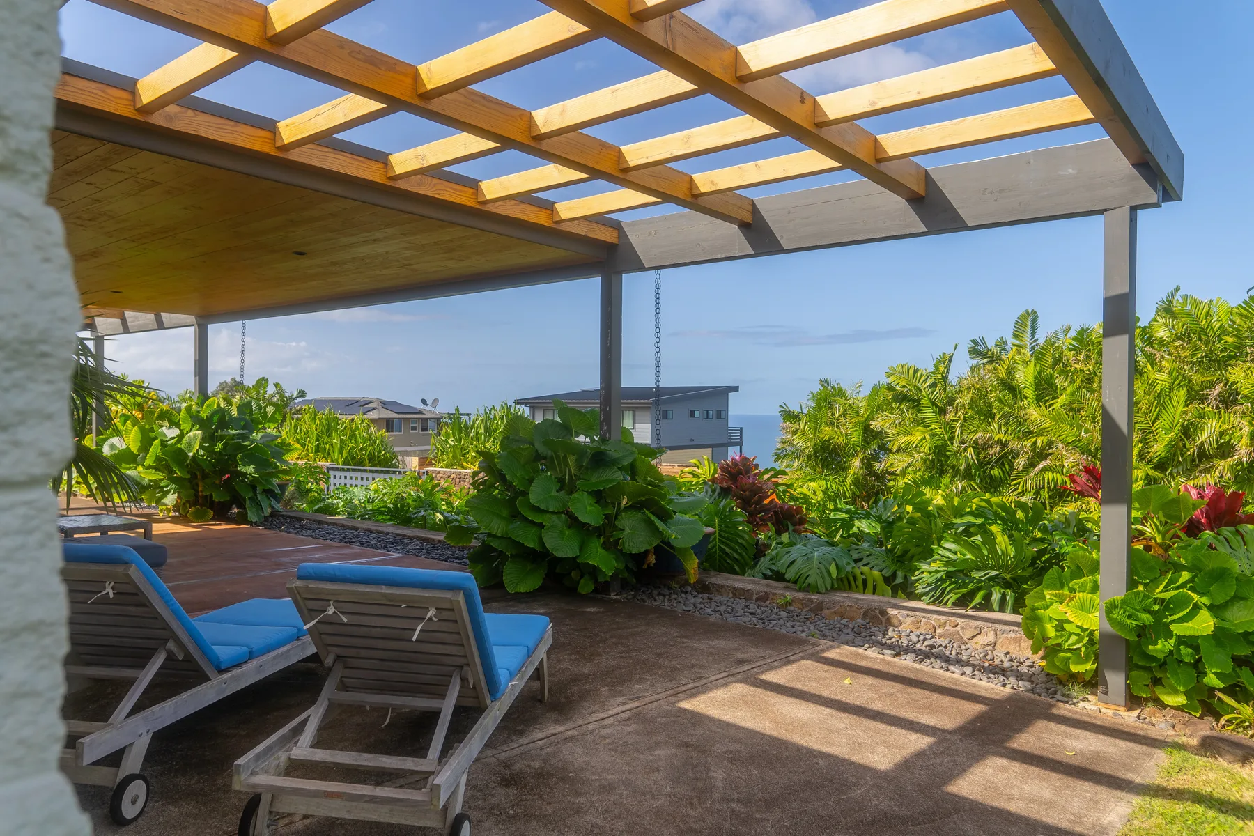 Un patio exterior sombreado con asientos de descanso y una pérgola de madera da a una vegetación frondosa.