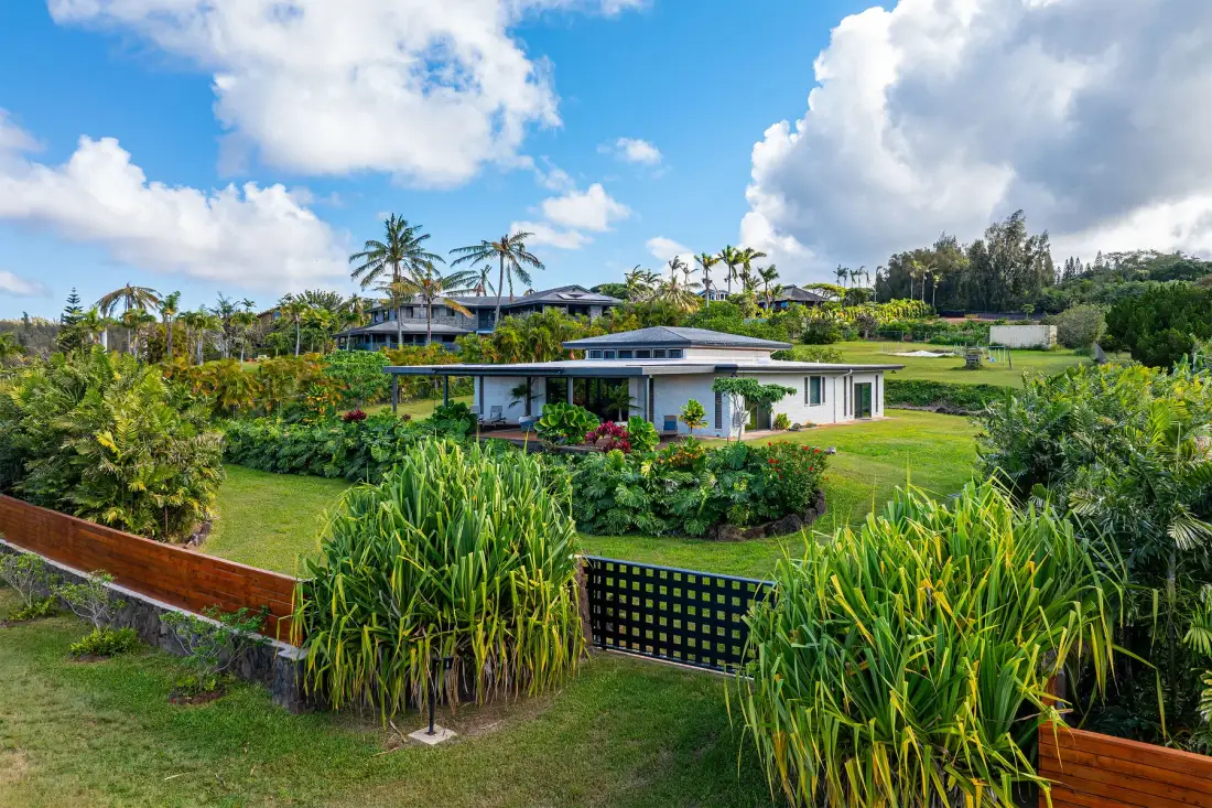 Una casa moderna de poca altura está rodeada de exuberantes jardines tropicales bajo un cielo brillante y nublado.
