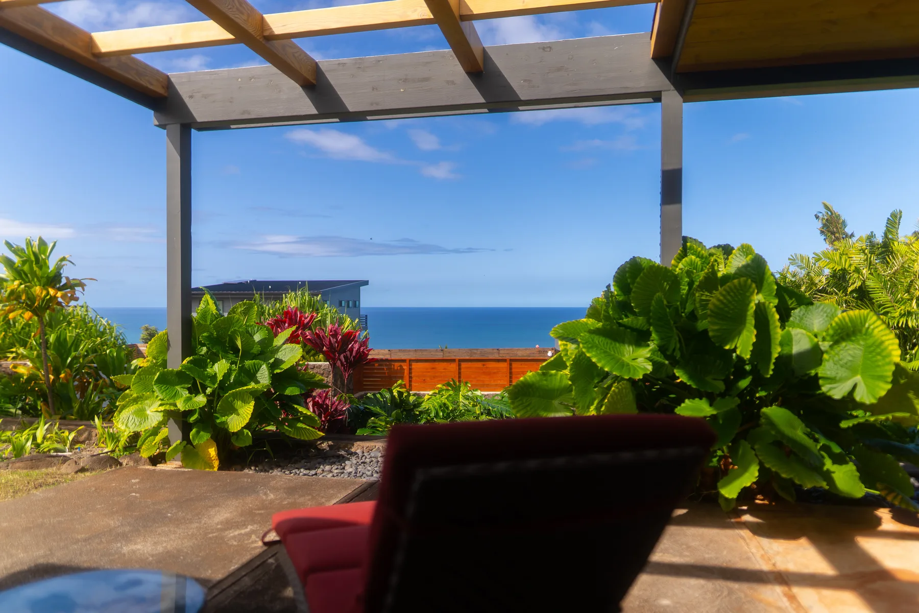 Una zona de estar exterior a la sombra tiene vistas al océano y está rodeada de plantas frondosas.