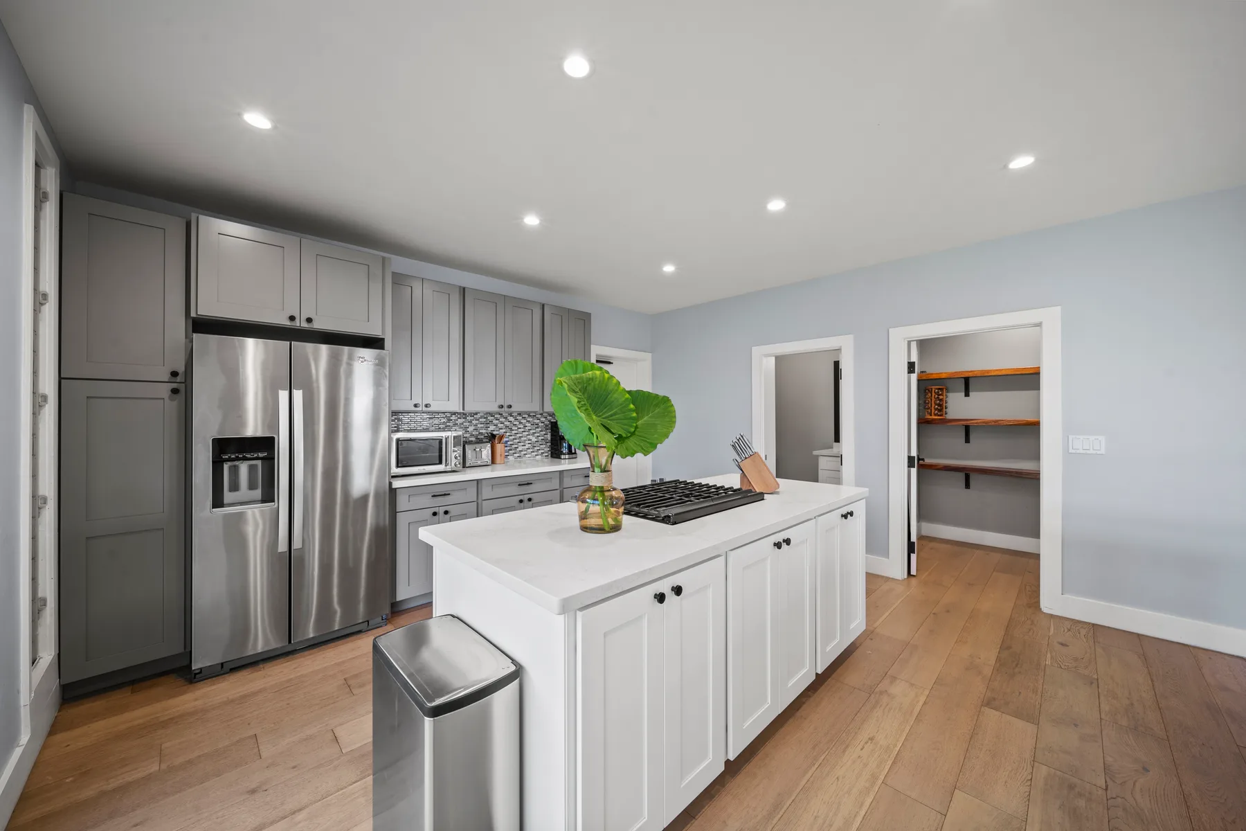 Una cocina luminosa con gabinetes grises, electrodomésticos de acero inoxidable y una isla blanca.
