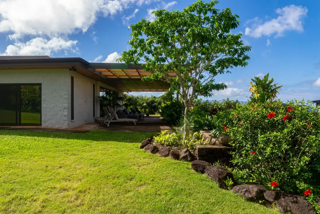 Una casa moderna se abre a un patio cubierto junto a un jardín cuidado.