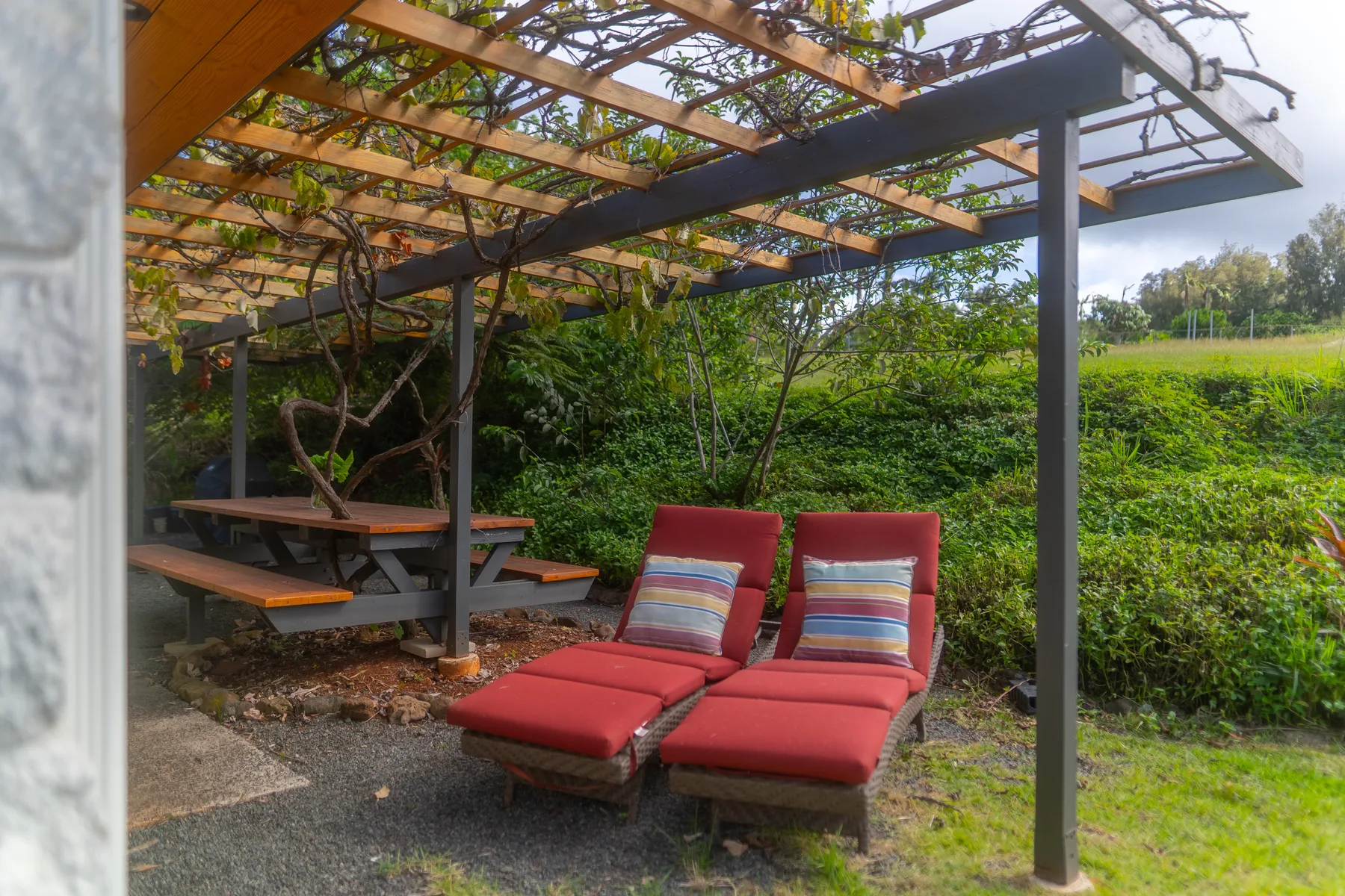 Una zona de estar al aire libre bajo una pérgola de madera, con dos sillones rojos.