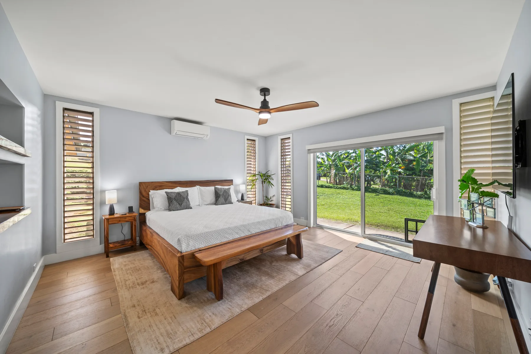 Un dormitorio luminoso con una cama de madera frente a grandes ventanas que dan a un jardín.
