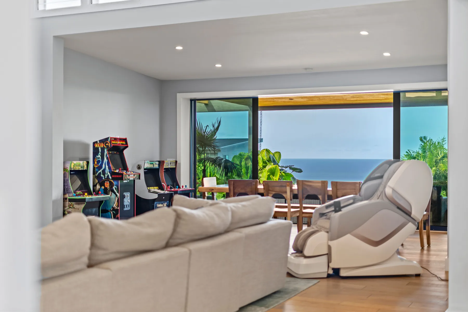 Una sala de estar con asientos y juegos arcade, abierta a un comedor con vistas al mar.