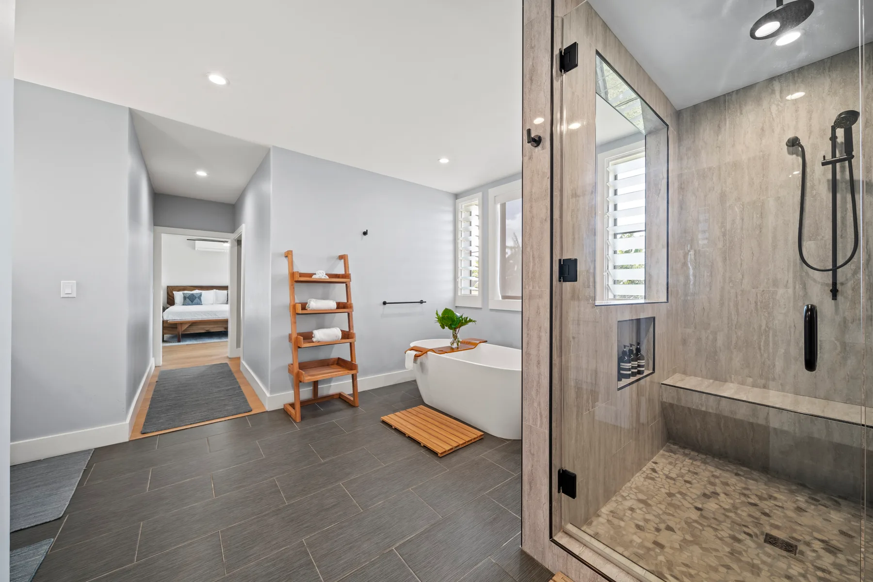 Un baño moderno con bañera, ducha abierta y estantería de madera.