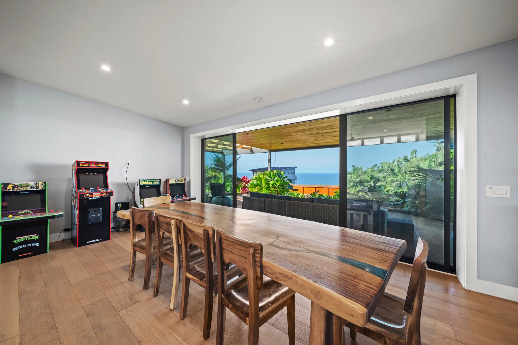 Un comedor con una larga mesa de madera y juegos arcade junto a puertas de vidrio.