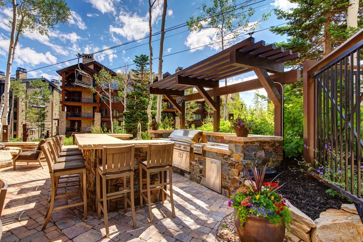 Un comedor al aire libre con una mesa de madera bajo una pérgola, rodeado de vegetación.