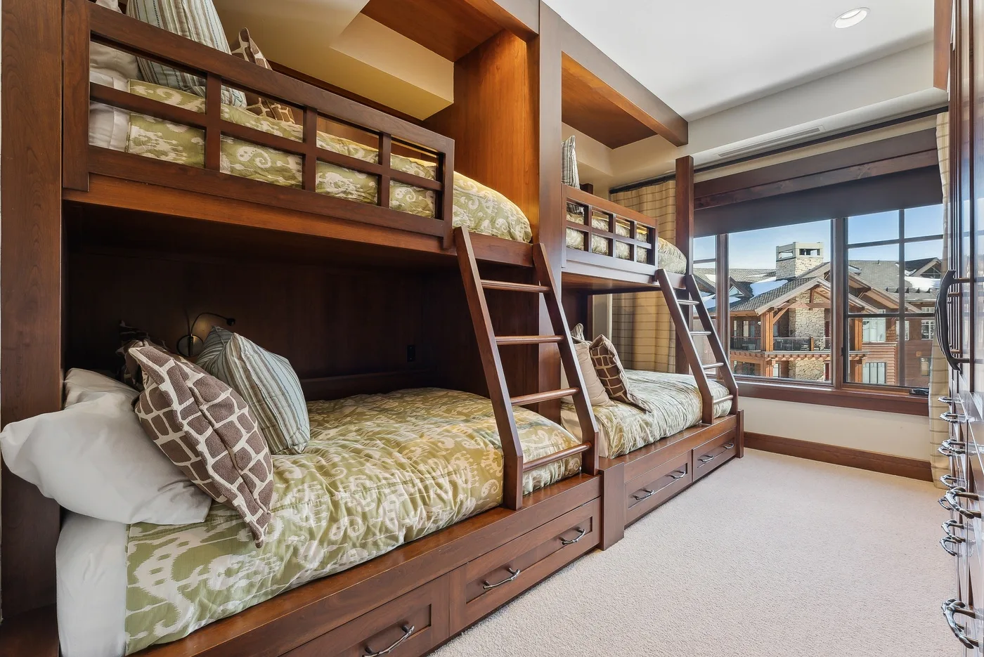 Un dormitorio con literas de madera y grandes ventanas con vistas a edificios cercanos.