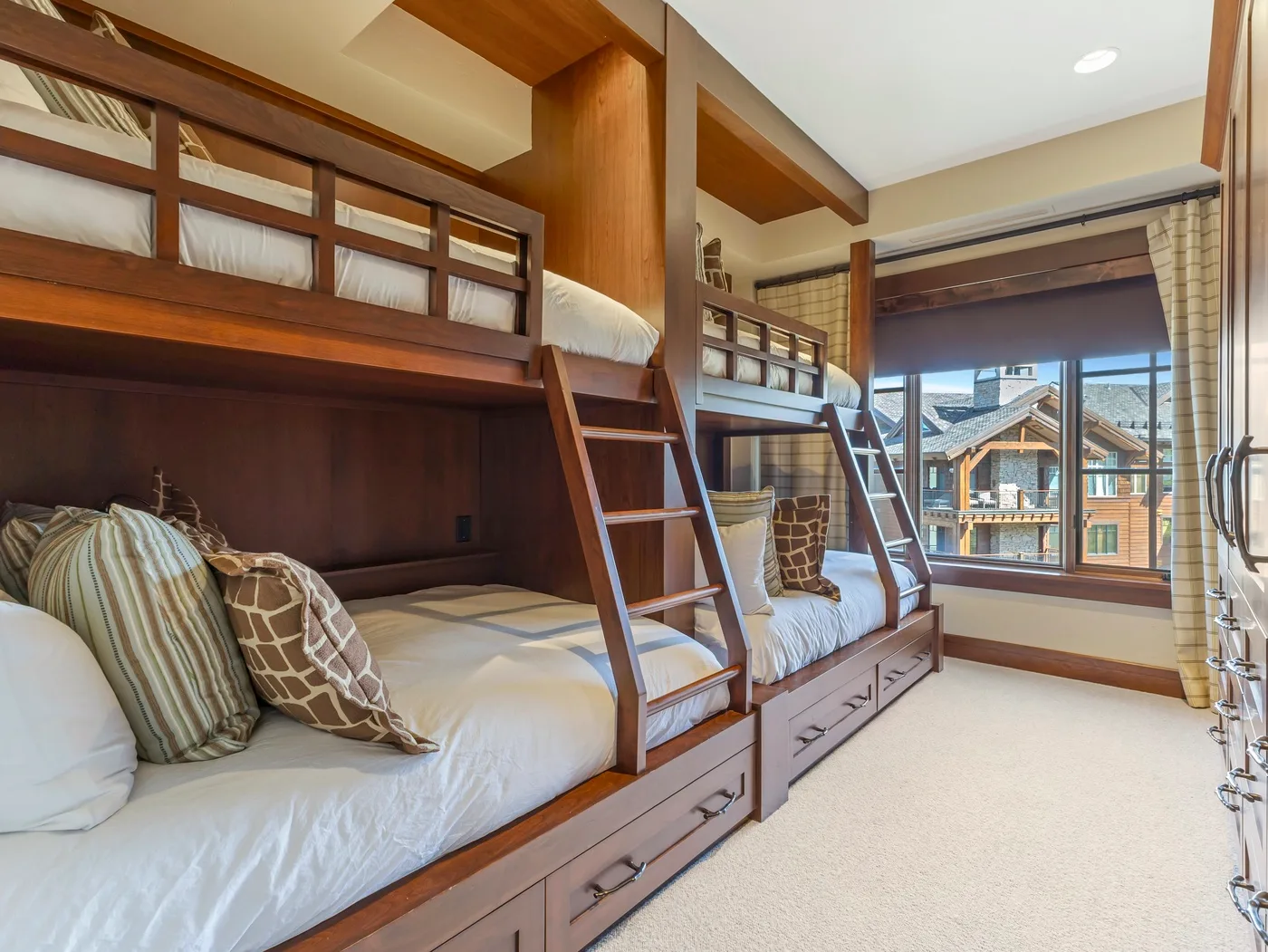 Dormitorio con literas empotradas y una ventana grande con vista a edificios cercanos.