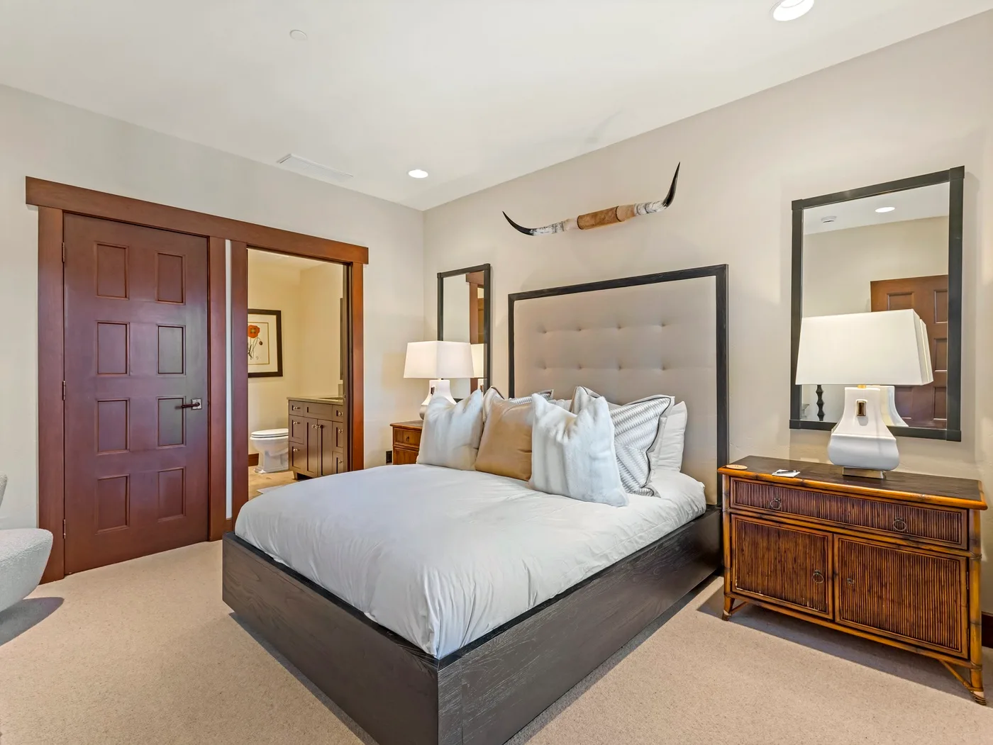 Un dormitorio con una cama bien tendida, lámparas de noche y una cómoda de madera.