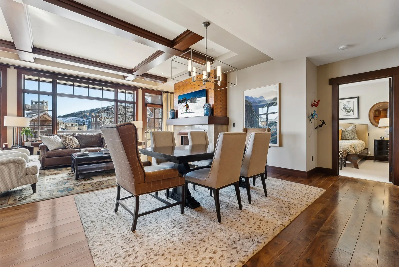 Comedor con mesa y asientos junto a una sala de estar con grandes ventanas.