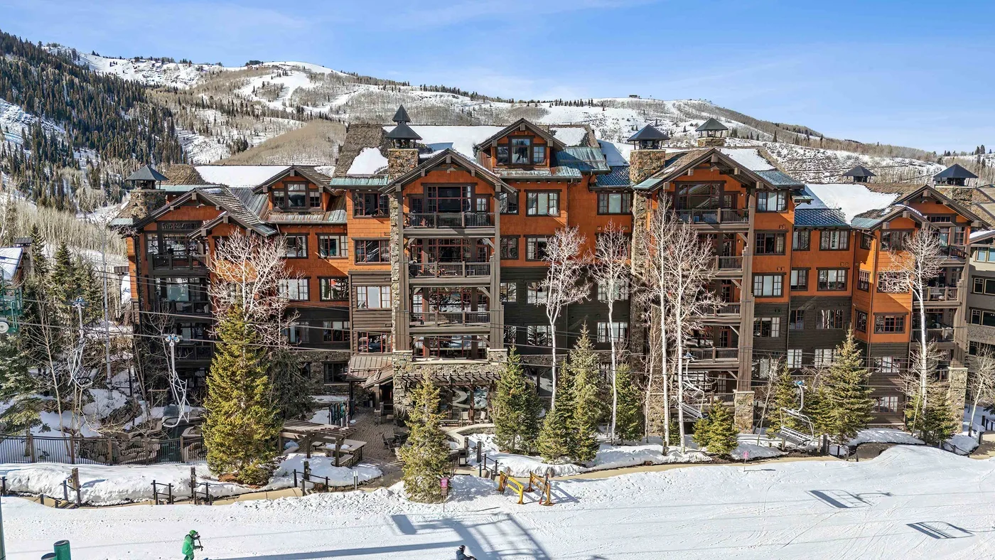 Un gran edificio de estilo albergue se alza junto a una pista nevada, bajo un paisaje montañoso.
