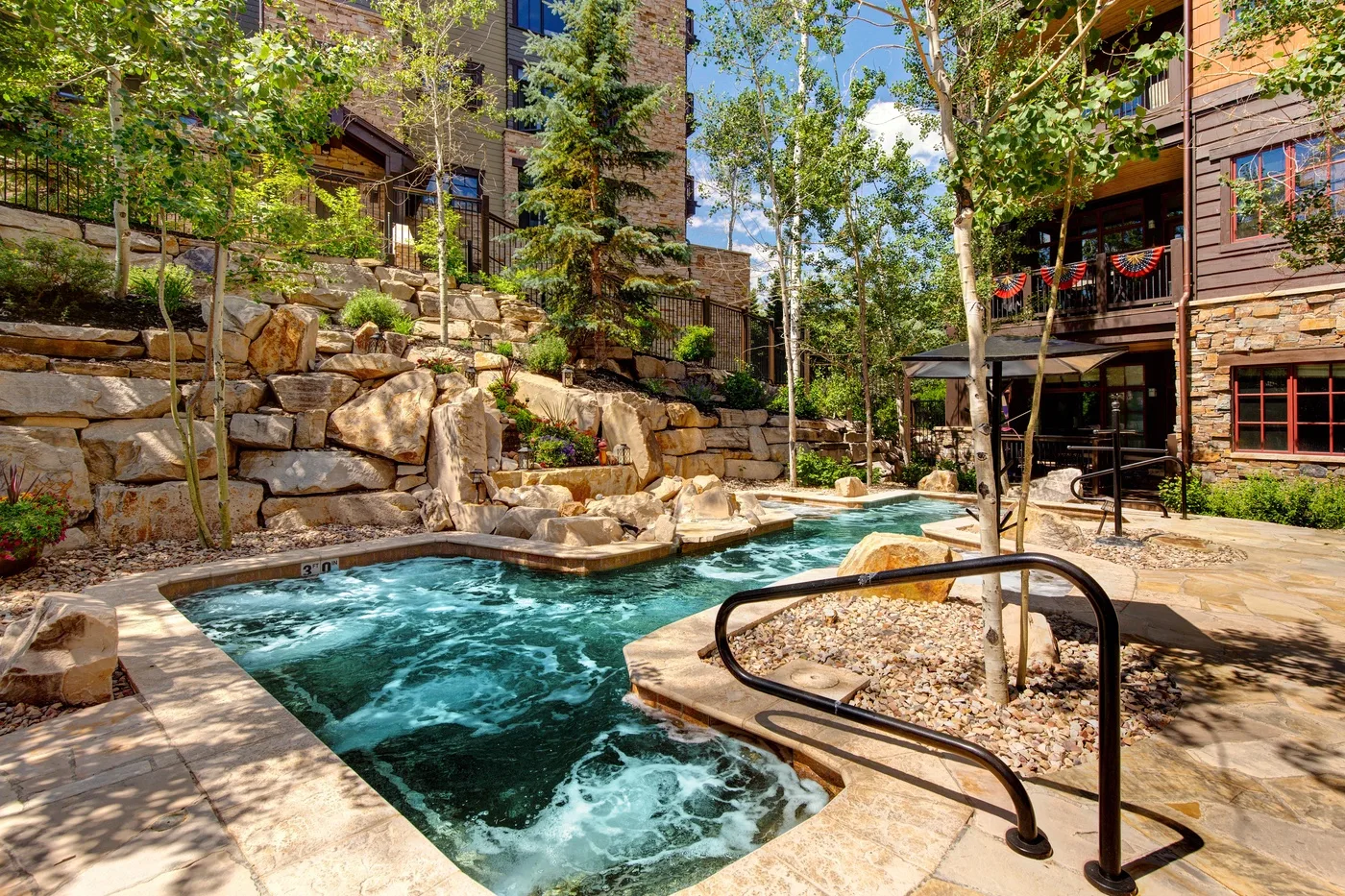 Una piscina al aire libre está rodeada de jardines de piedra, árboles y edificios de varias plantas.