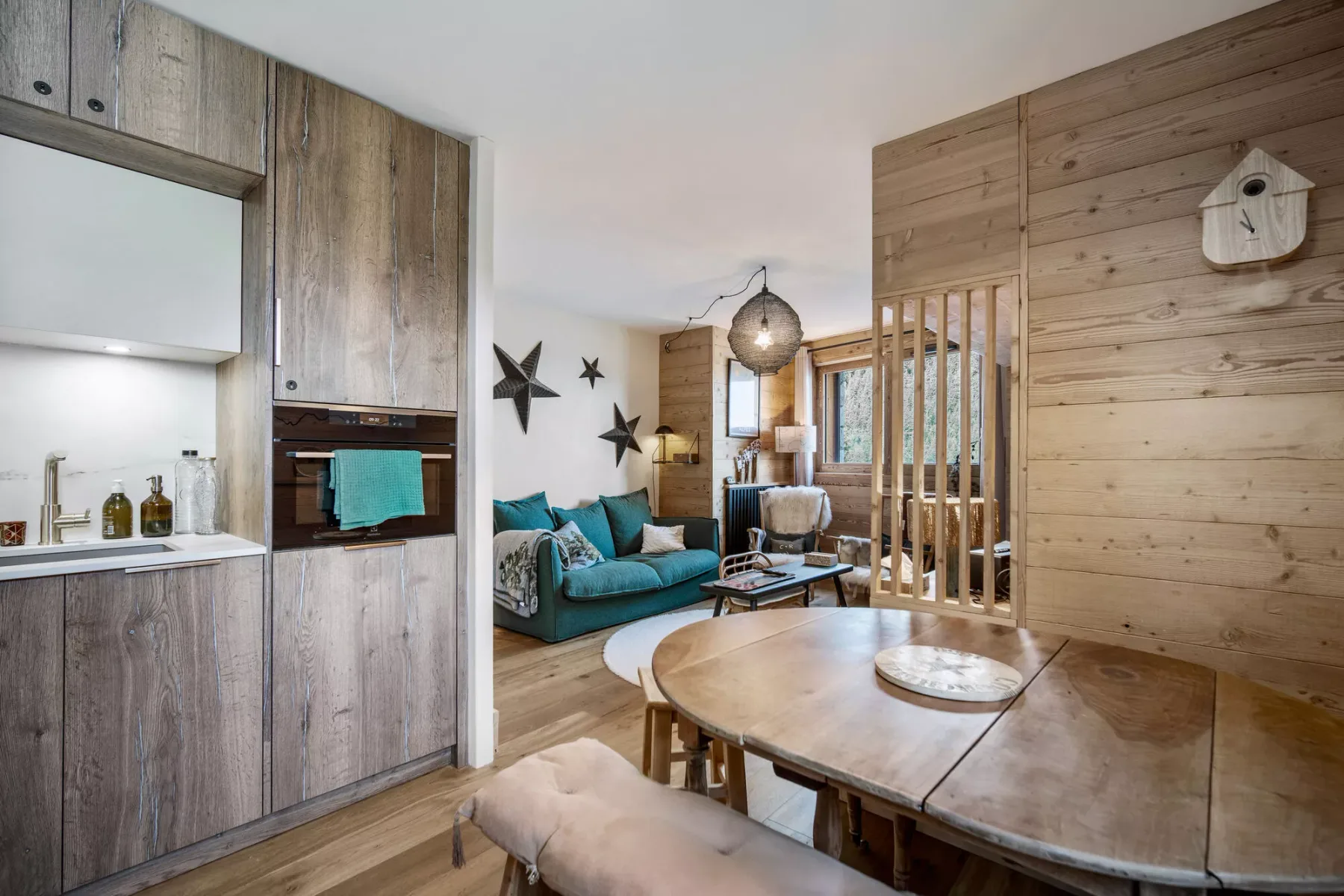 An open-plan living and dining area with a teal sofa and wooden table.