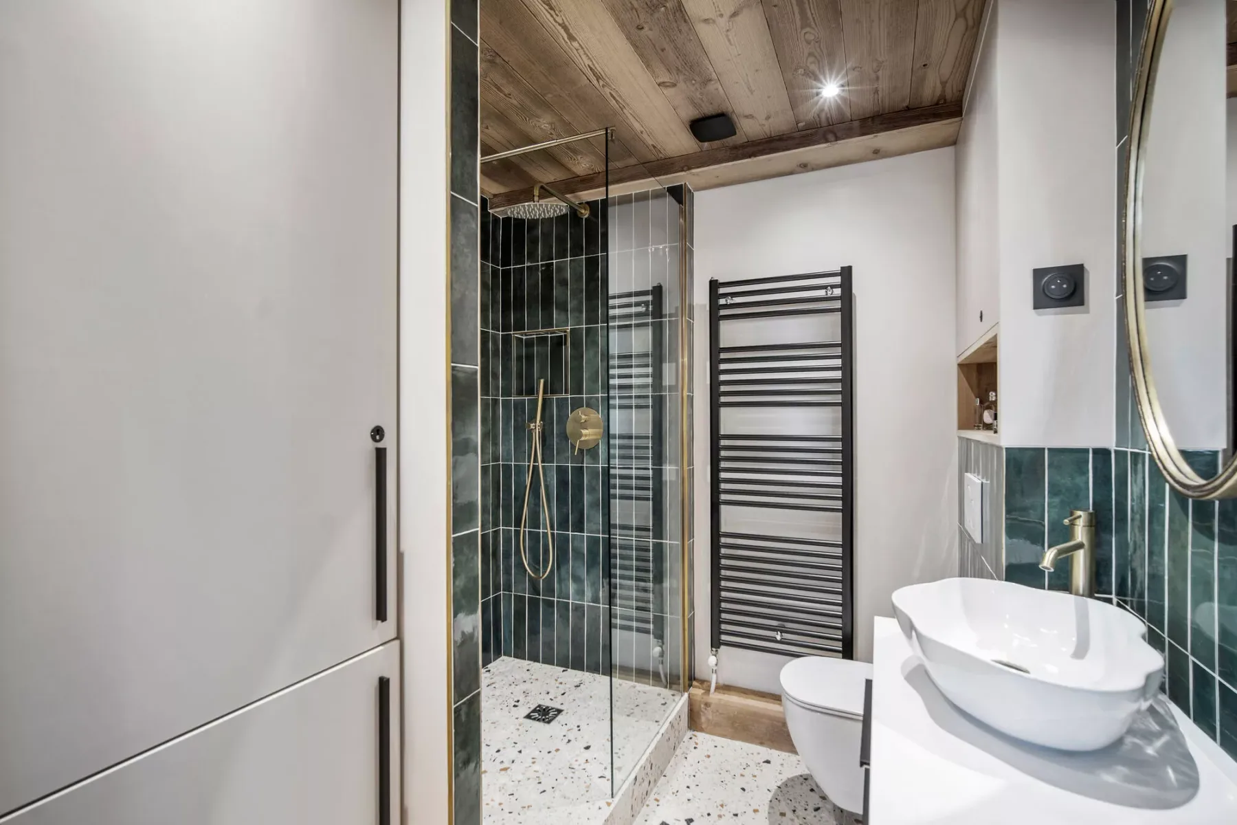 A bathroom with a glass shower, sink, and wall-mounted towel warmer.