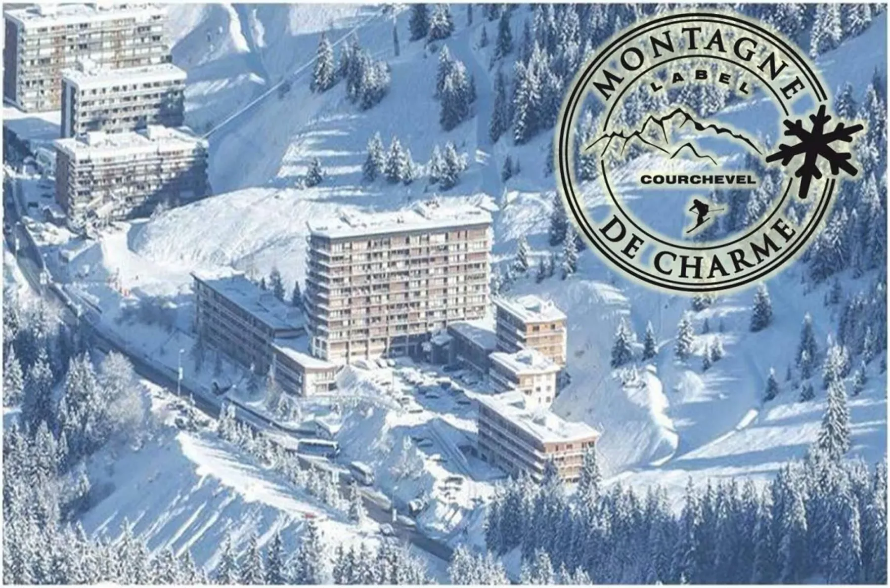 Aerial view of snow-covered buildings among forested mountain slopes.