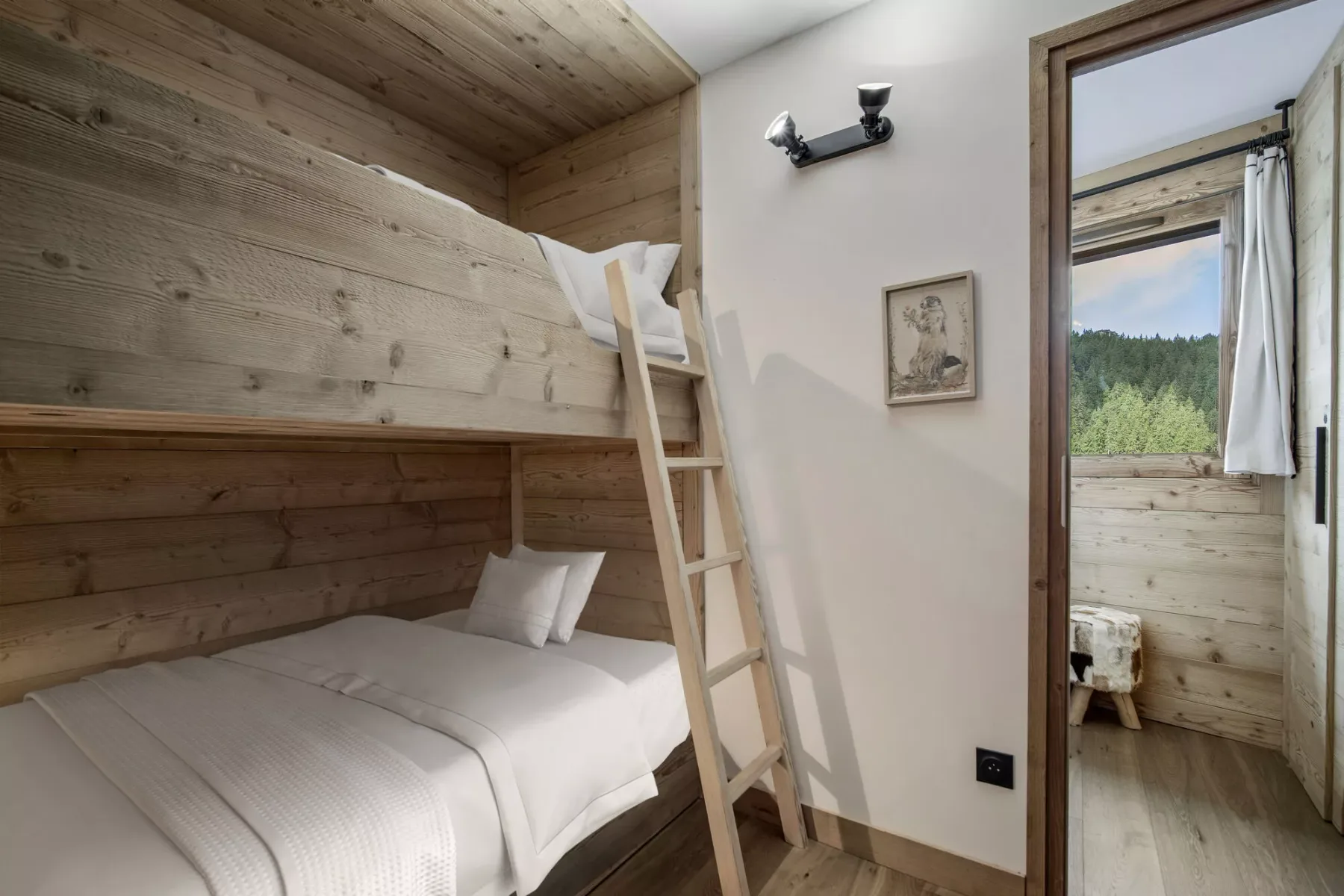 A wood-paneled bedroom with a bunk bed and a doorway opening to a bright adjoining room.
