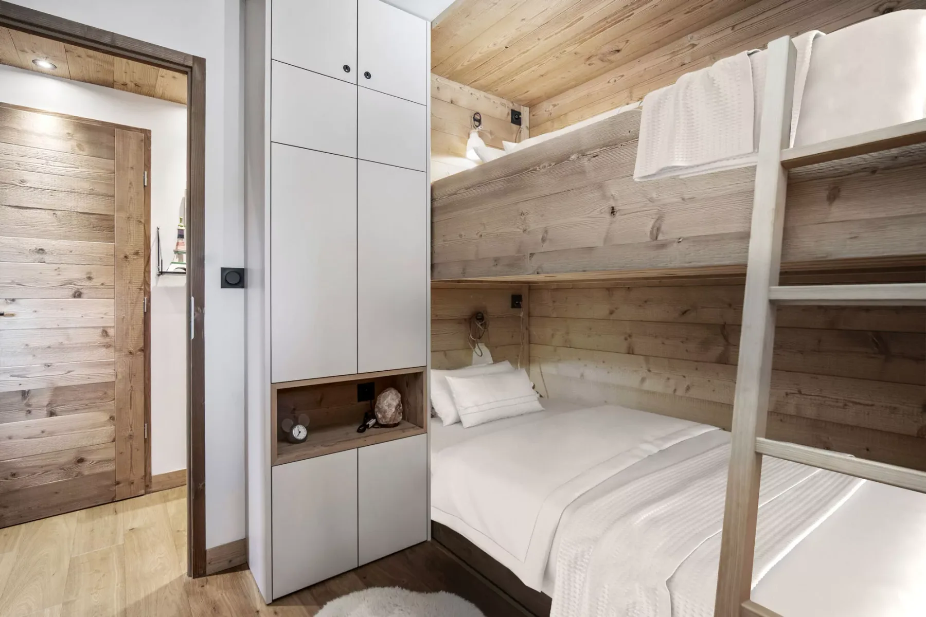 A bedroom with a wooden bunk bed and white bedding.