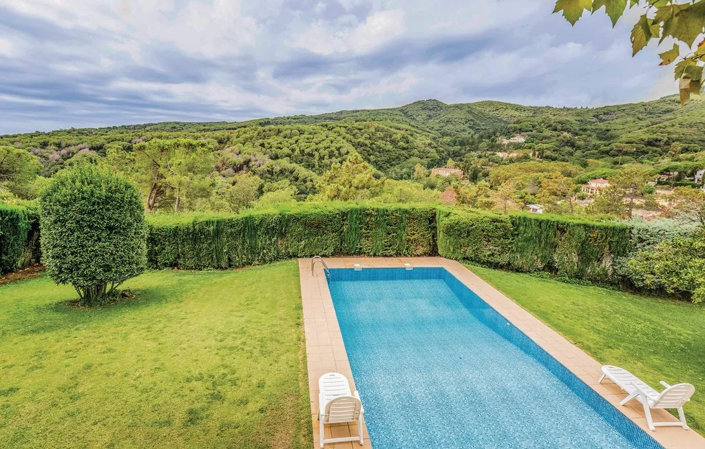 Una piscina al aire libre está en un jardín con césped y colinas verdes al fondo.