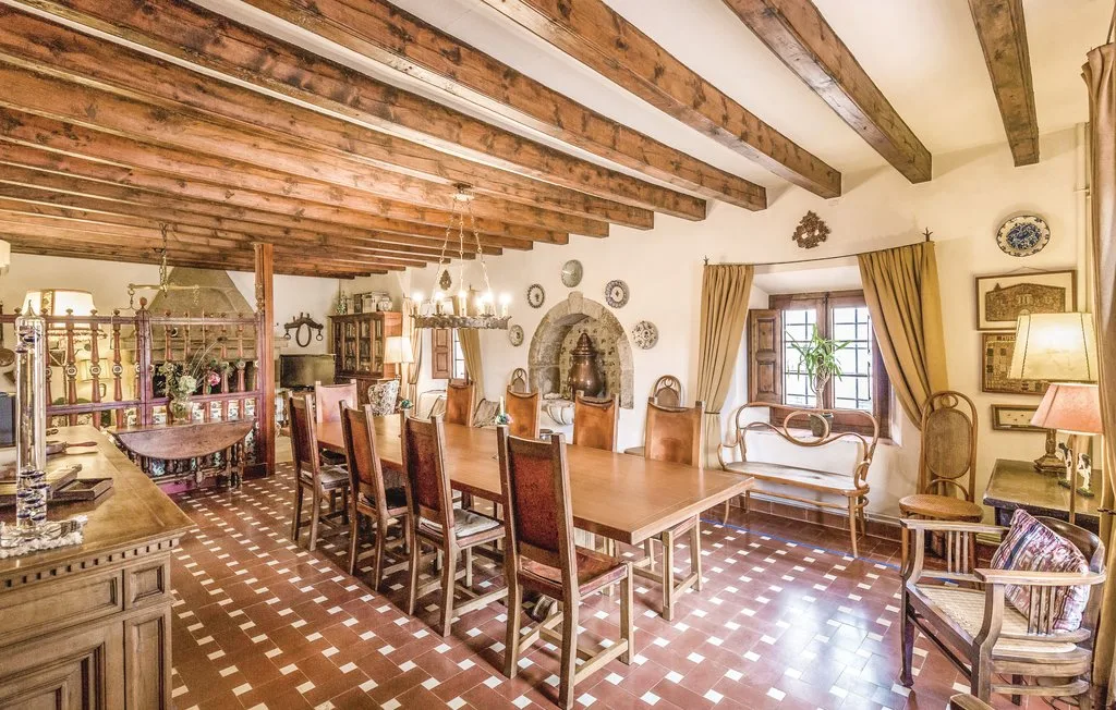 Un amplio comedor con una larga mesa de madera bajo vigas vistas en el techo.
