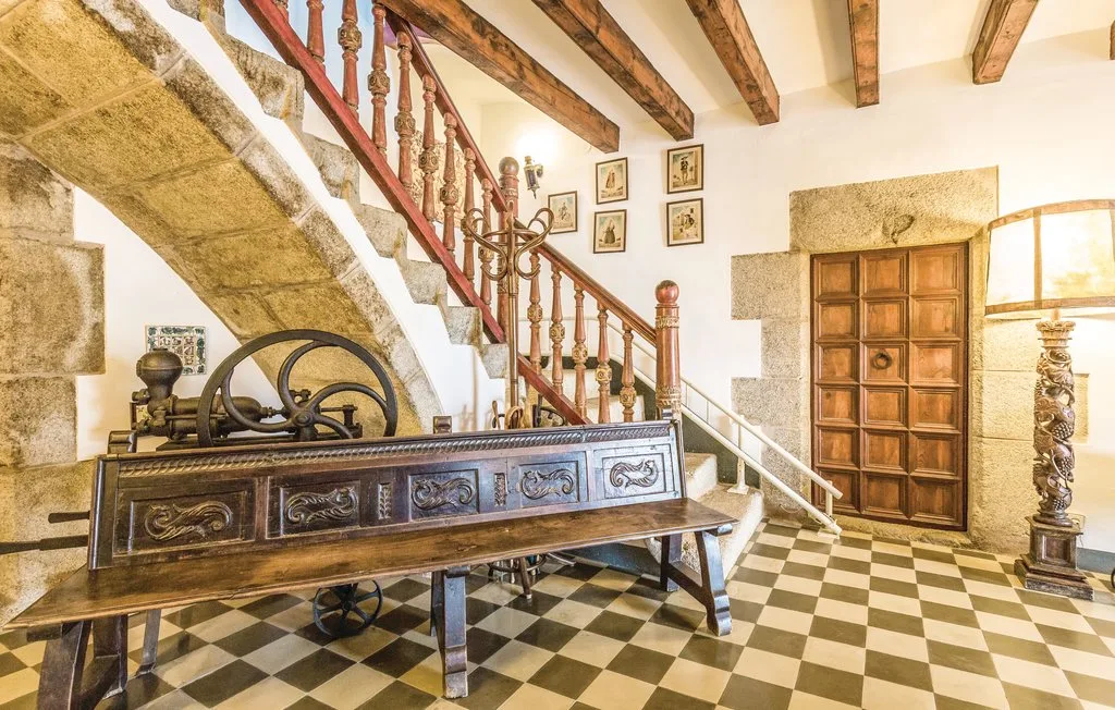 Una escalera de piedra y madera sube sobre un recibidor embaldosado con una mesa larga.