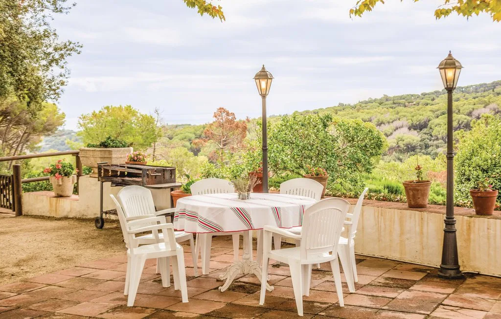 Una zona de comedor al aire libre con mesa y asientos blancos da a colinas verdes.