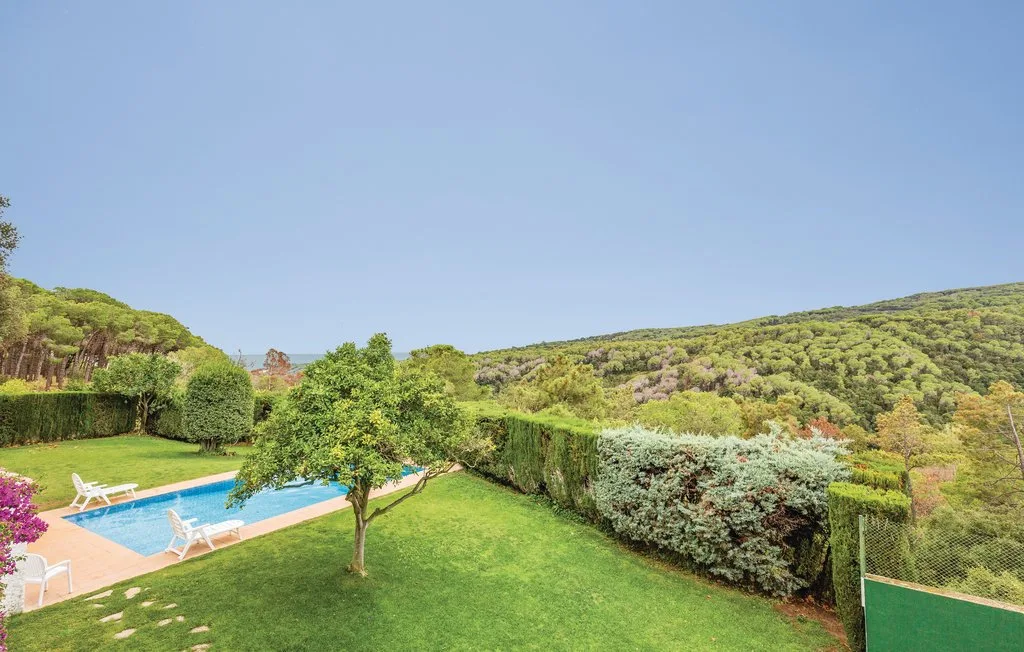 Un jardín con piscina, césped y colinas alrededor.